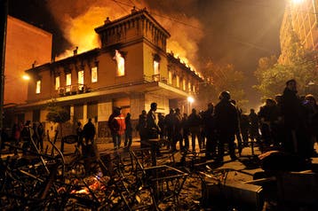 Gente mirando mientras se quema un edificio en Atenas, Grecia